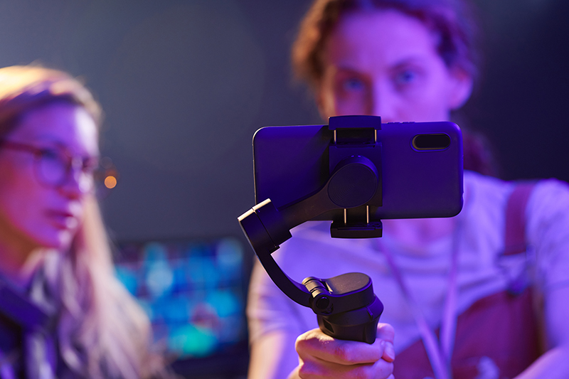 Close up of young woman holding smartphone with stabilizer and filming video for content creation, copy space