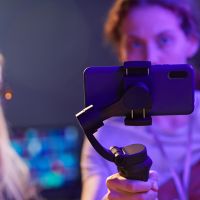 Close up of young woman holding smartphone with stabilizer and filming video for content creation, copy space